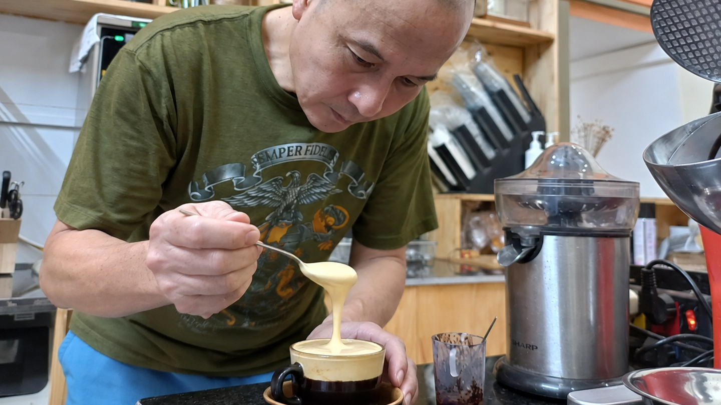 Cafe owner prepares egg coffee by pouring thick foam over a cup in Hanoi.