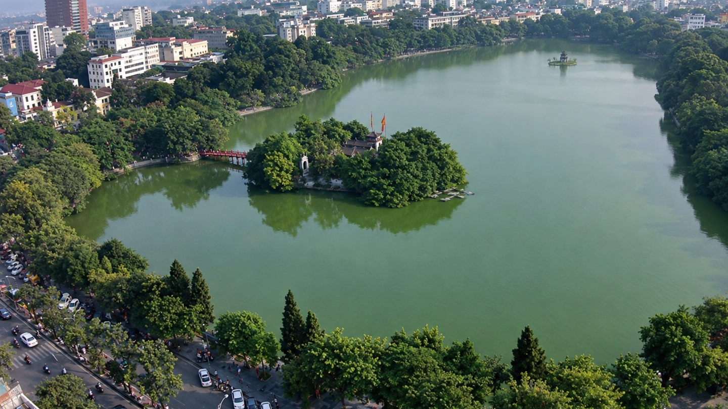Aerial view of Hoan Kiem Lake and its tree-covered island, with Hanoi's Old Quarter along the shore.