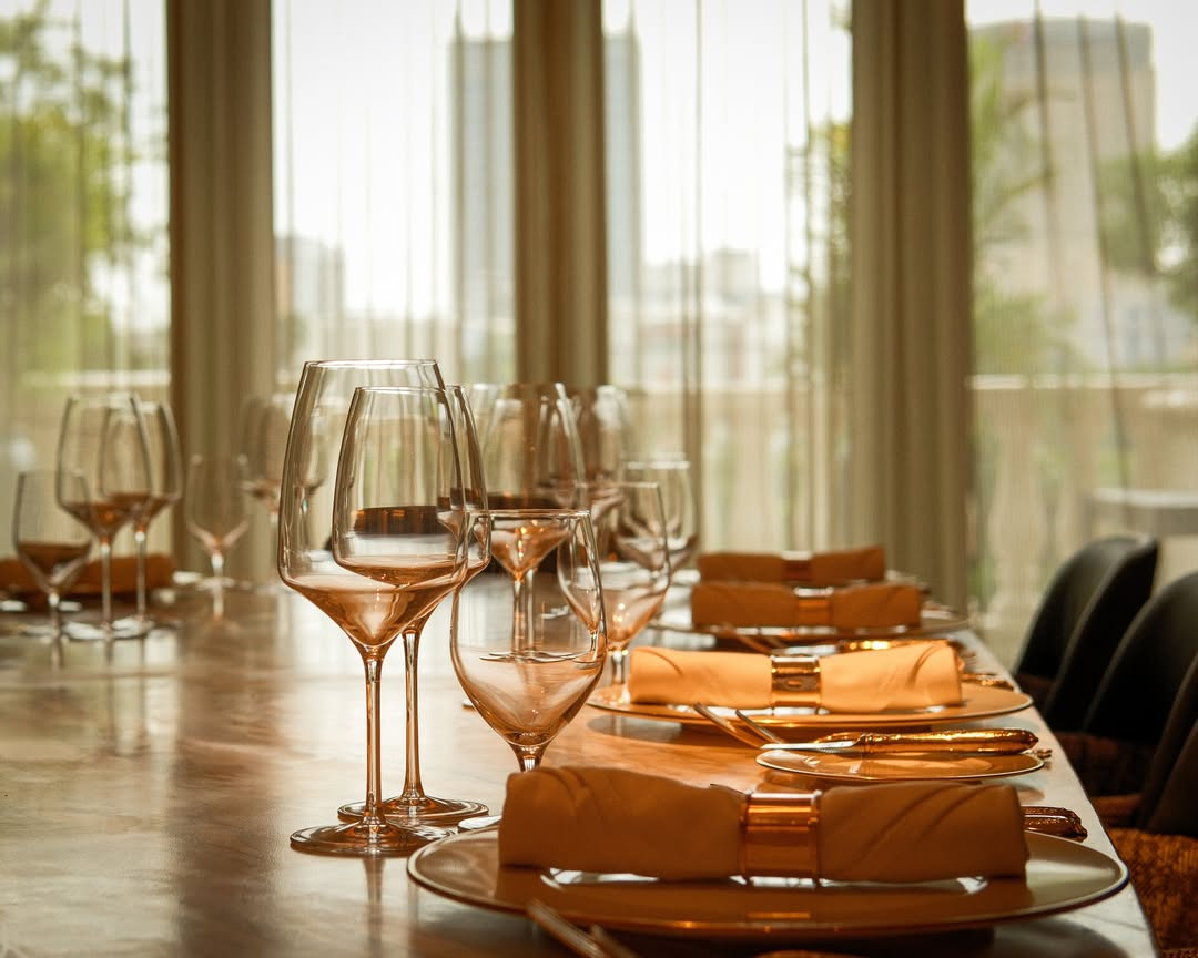Fine-dining table set with plates and wine glasses beside tall windows at The Theodore Hanoi.