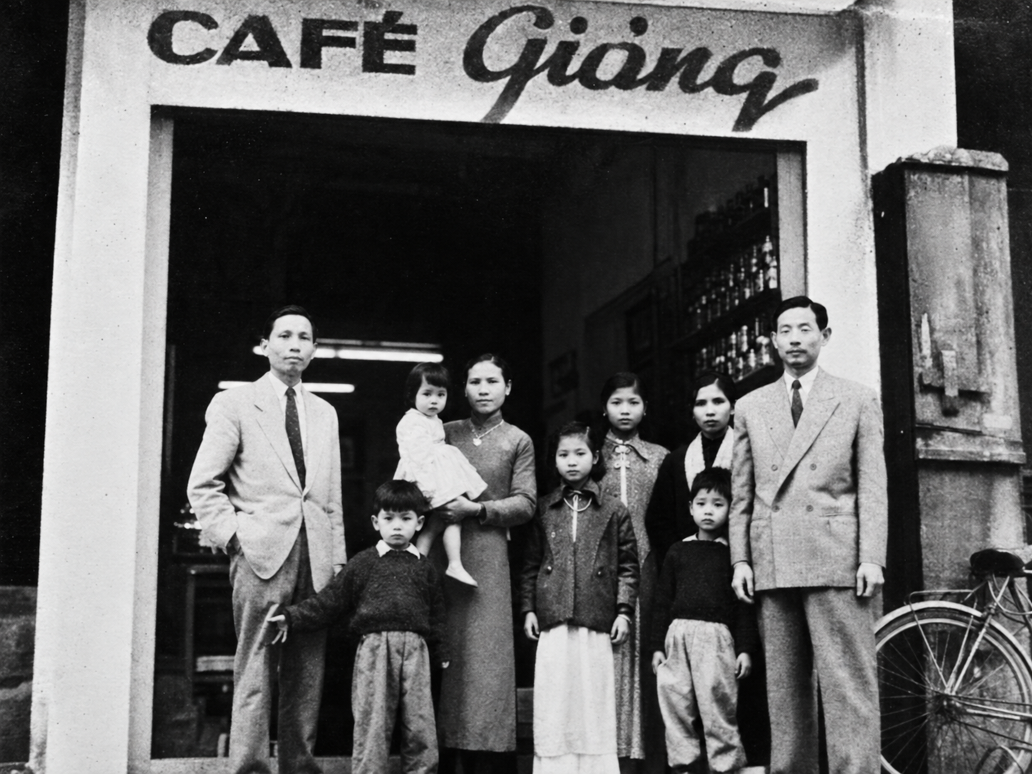 Black-and-white group portrait outside a traditional Hanoi café, illustrating the history of Cafe Giang.
