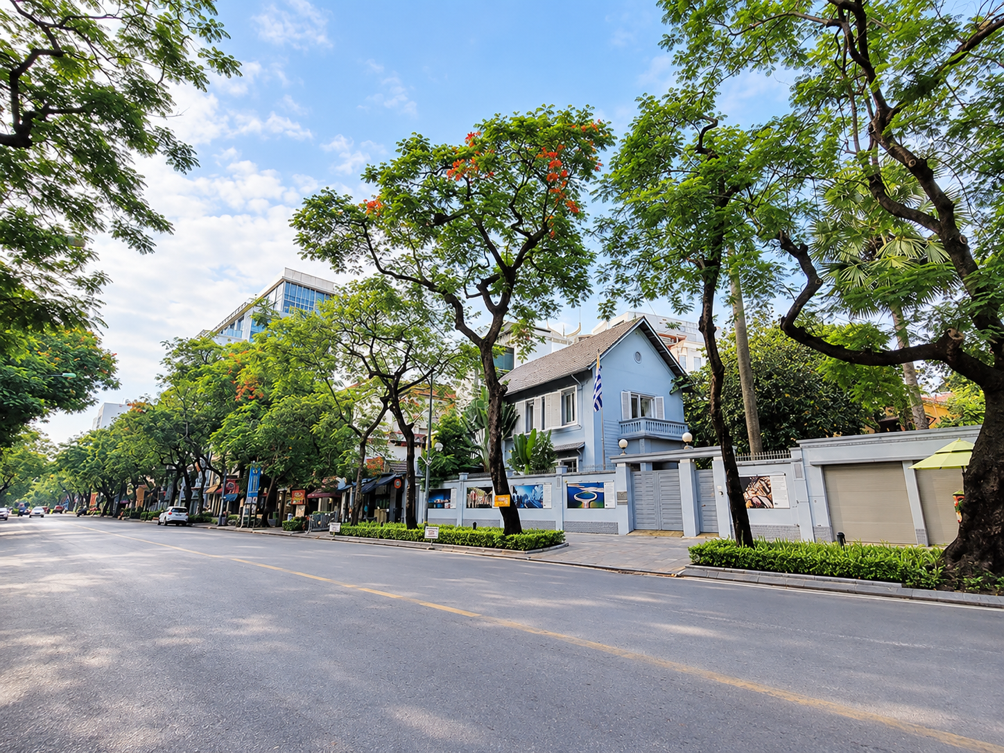 Quiet, tree-lined street in Hanoi's French Quarter beside a pale colonial-style building.