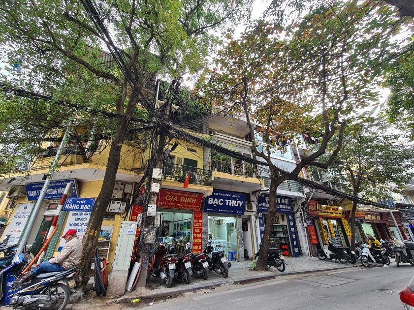 Tree-lined Old Quarter street with shopfronts and parked motorbikes in Hanoi.