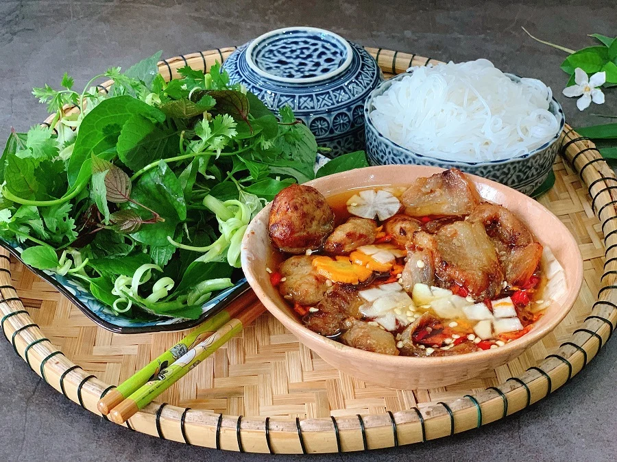 Bún chả with grilled pork, vermicelli and fresh herbs served on a woven tray.