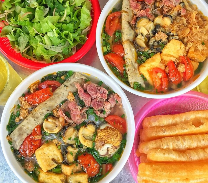 Bowls of bun oc and vermicelli with herbs set out on a Hanoi breakfast table.