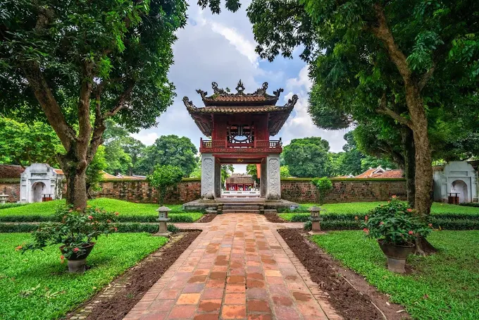 Red-roofed entrance pavilion at the Temple of Literature seen from a garden path.