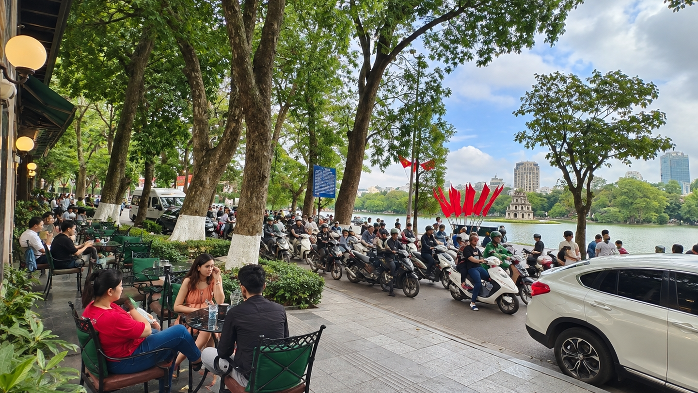 Outdoor seating beneath trees along the West Lake shore in Hanoi.