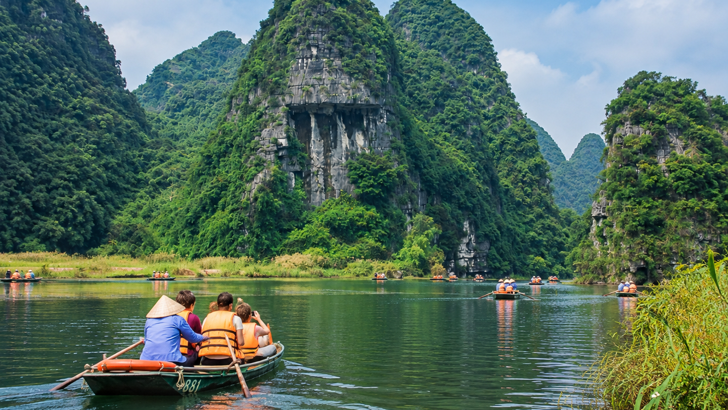 Visitors ride a small boat across a green karst lake on a day trip from Hanoi.