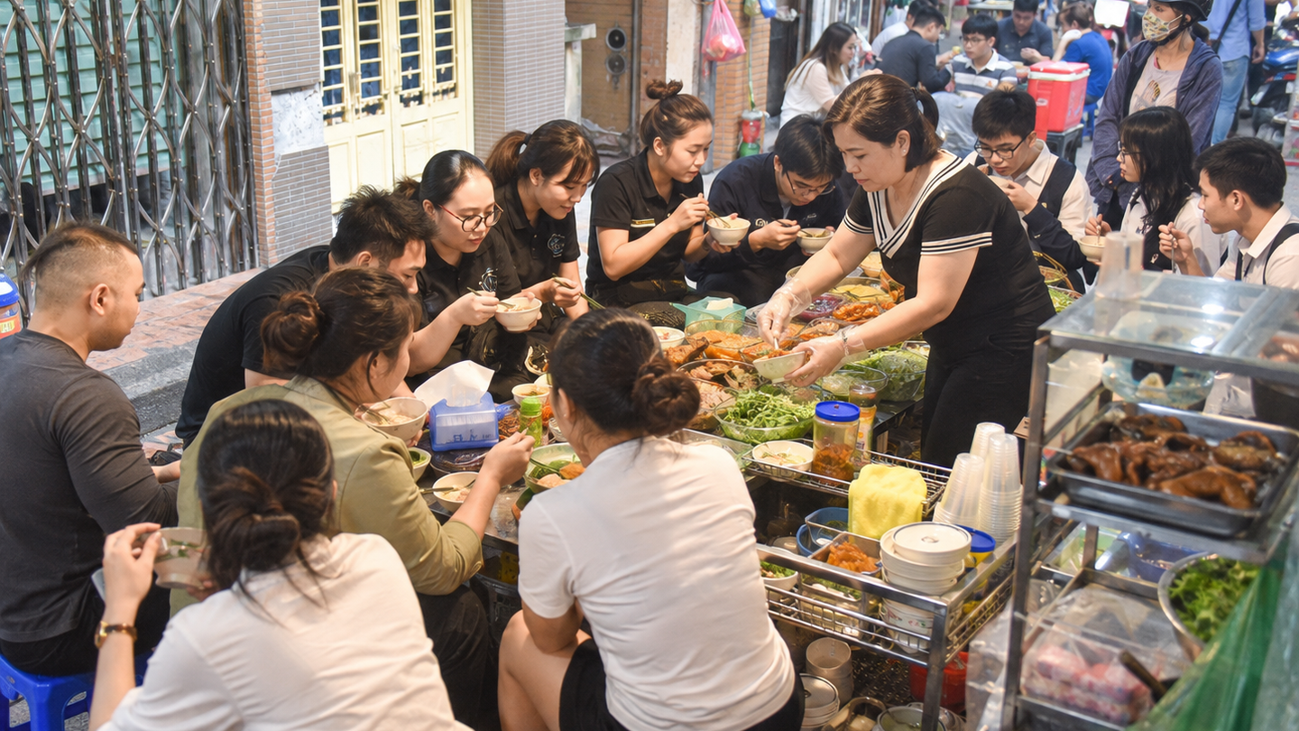A crowded Hanoi street-side café where diners share breakfast at communal tables.