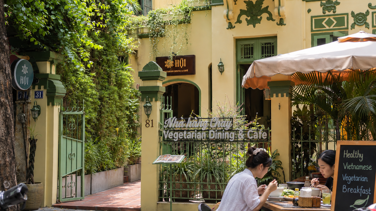 Entrance to a leafy vegetarian café in Hanoi, with outdoor seating by a French-style facade.