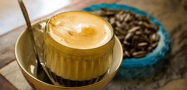 A glass of creamy egg coffee beside roasted coffee beans in Hanoi.