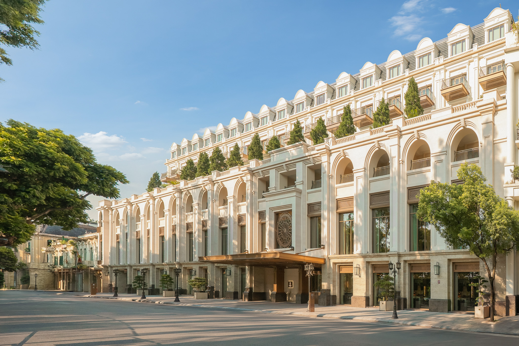The Theodore Hanoi’s pale French-style exterior on a tree-lined street by day.
