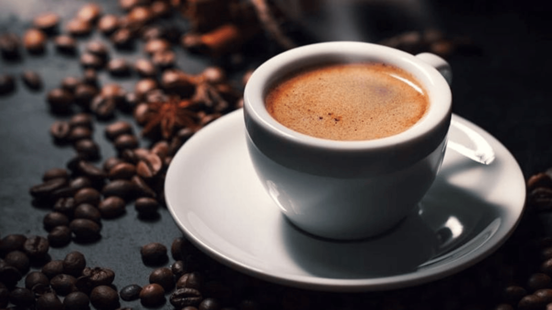 Cup of black Vietnamese coffee on a saucer beside roasted coffee beans.